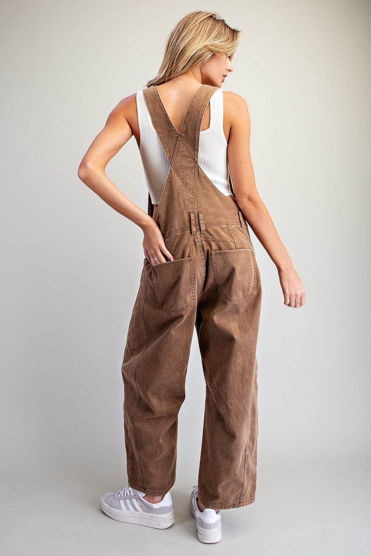 Back view of woman in brown mineral wash barrel overall with crisscross back design, large front pocket, and casual style