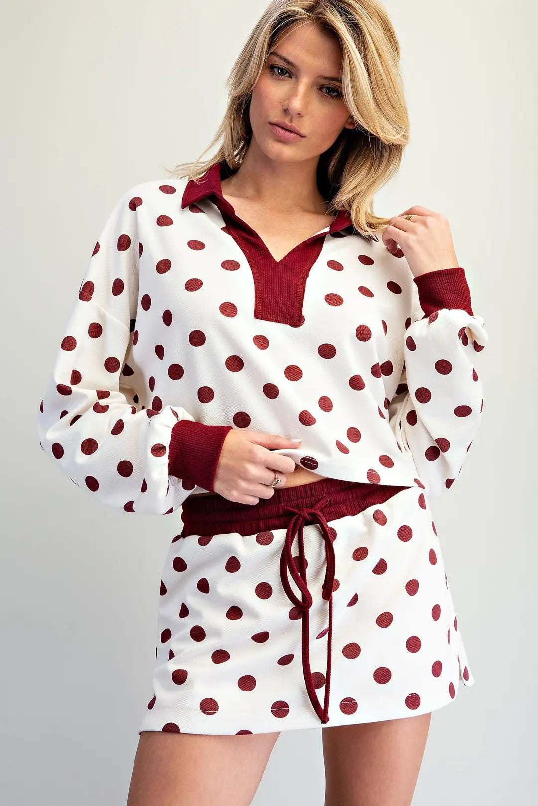 Women's ivory and burgundy polka dot two-piece set featuring a long-sleeve collared pullover top and matching drawstring mini skirt.