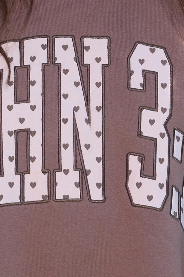 Close-up of mauve sweatshirt displaying 'John 3:16' text with white letters outlined in black, decorated with small heart patterns for Christian faith apparel