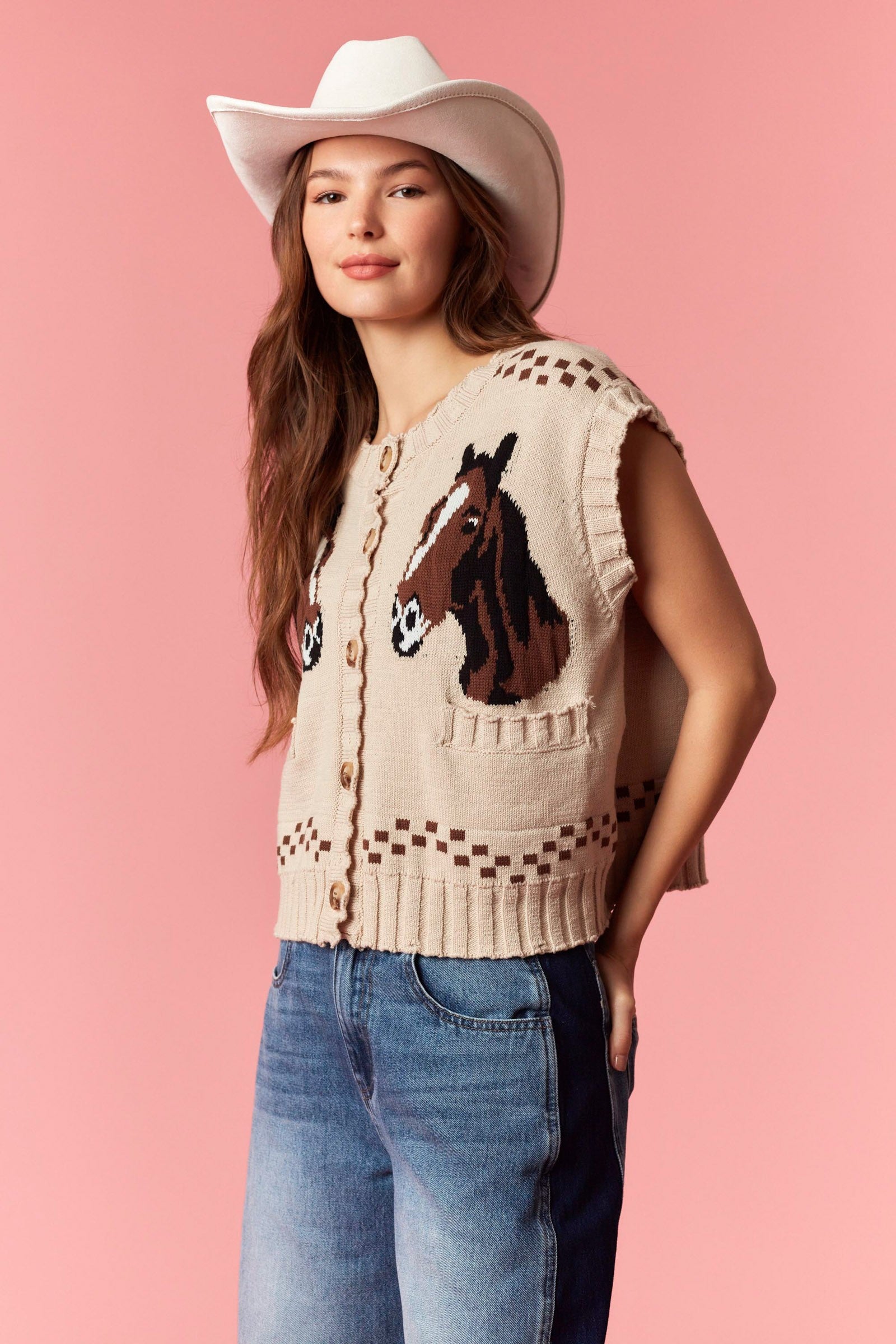 Cream knitted vest with a horse motif, button-front closure, sleeveless design, and decorative square patterns, styled with blue jeans