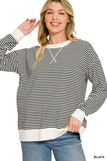 A woman wearing a black and white horizontally striped long-sleeve crewneck sweatshirt with white ribbed cuffs and hem, paired with blue jeans, on a white background.