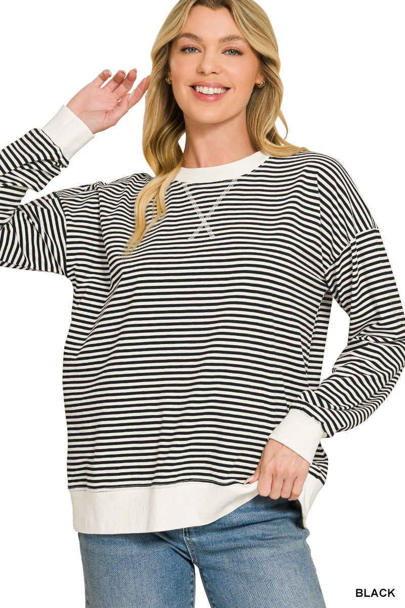 A woman wearing a black and white horizontally striped long-sleeve crewneck sweatshirt with white ribbed cuffs and hem, paired with blue jeans, on a white background.