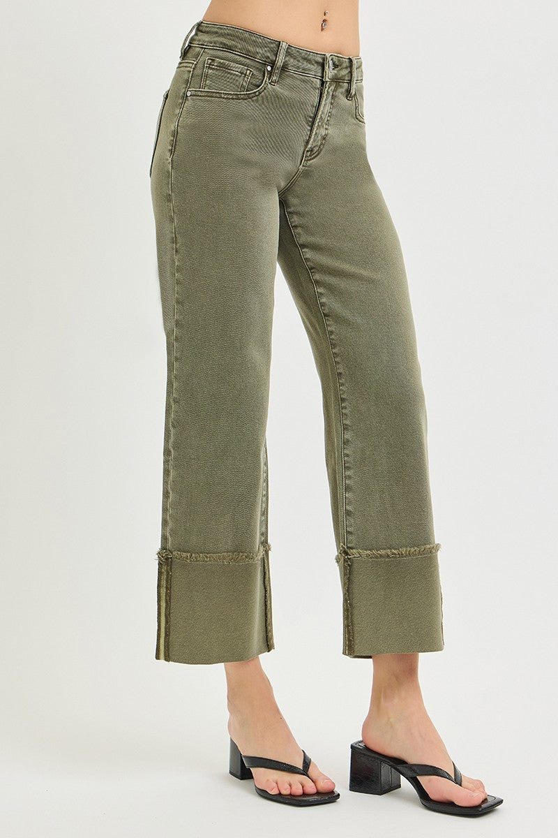 Close-up of olive green wide leg jeans with frayed cuffed hems, front zipper, belt loops, and relaxed fit, worn with heels