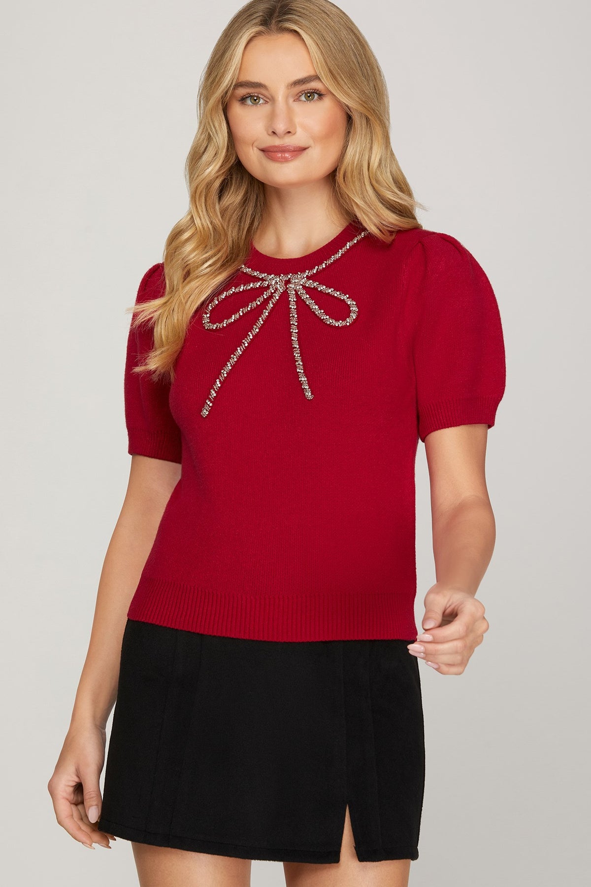 Close-up of the red sweater's rhinestone bow detail at the neckline, highlighting the beaded embellishments and elegant design.