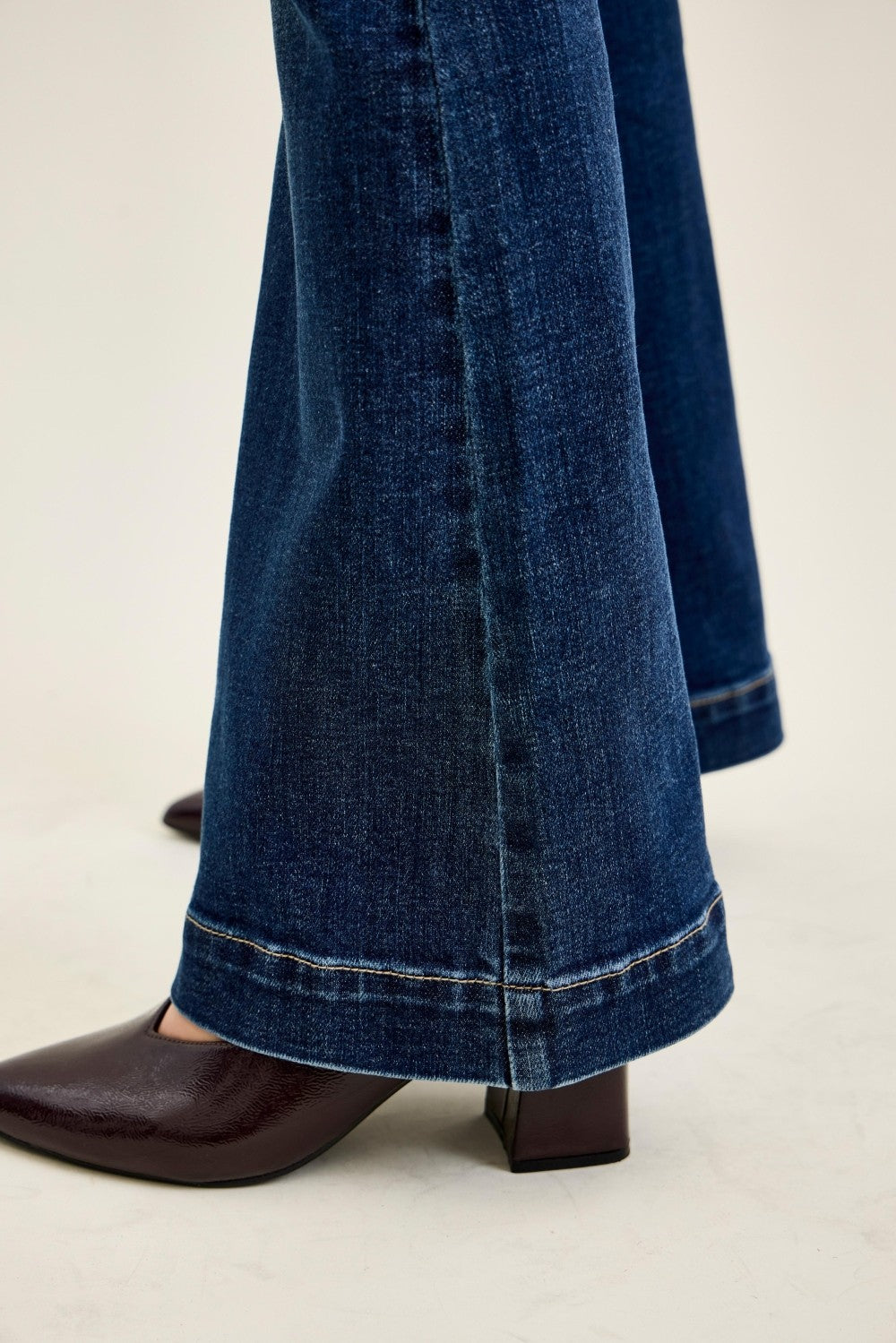Dark blue denim flared trousers with visible stitching at the hem, paired with pointed toe brown boots, showcasing a stylish wide-leg silhouette.