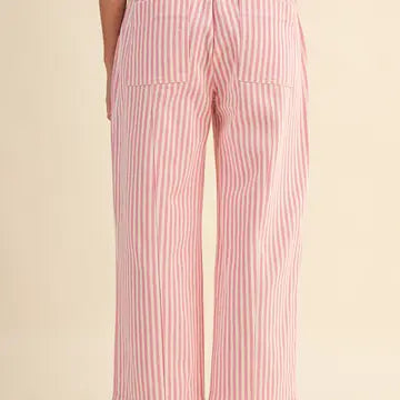 Pink and white vertically striped wide-leg pants shown from the back, featuring two large patch pockets, on a solid cream background.