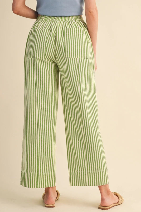 A person shown from the back wearing light green and white vertically striped wide-leg cropped pants, paired with a light blue top and tan flat sandals, against a plain beige studio background.