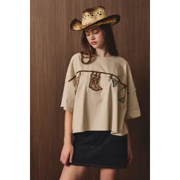 Women’s neutral beige western graphic T-shirt featuring cowboy boots and western accessories with a relaxed boxy fit.
