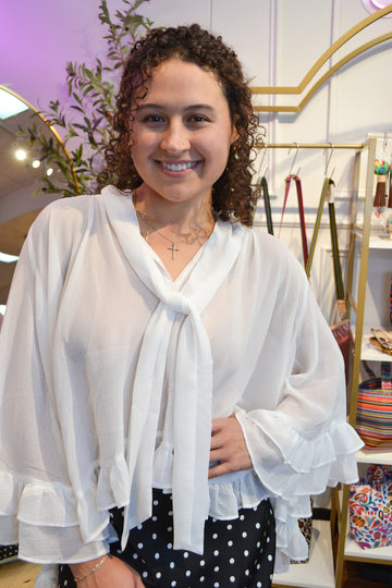 Women’s white ruffle blouse with a tie-neck bow, flowy bell sleeves, and lightweight chiffon fabric for an elegant look.
