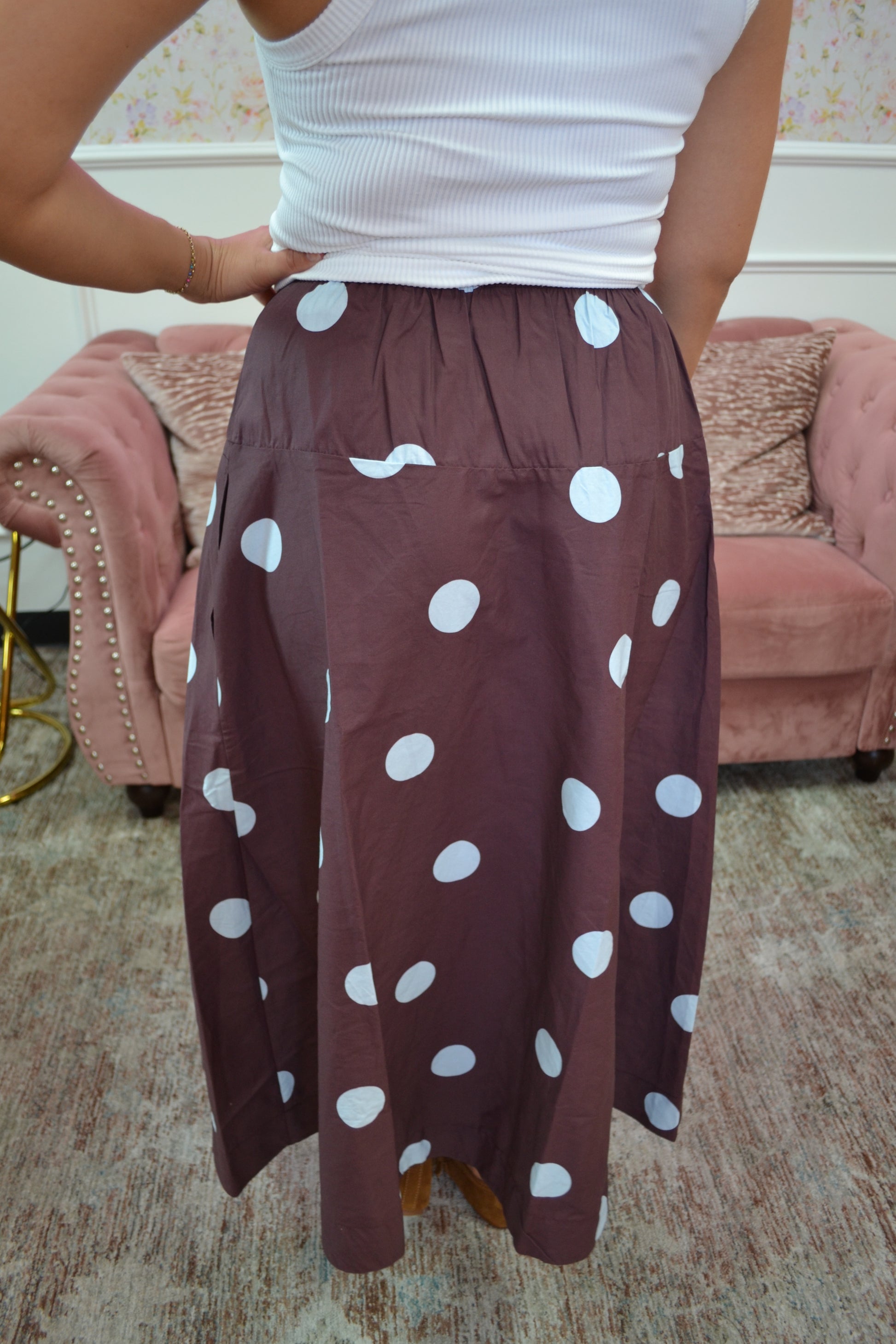 A person wearing a brown skirt with large blue polka dots, paired with a white ribbed tank top