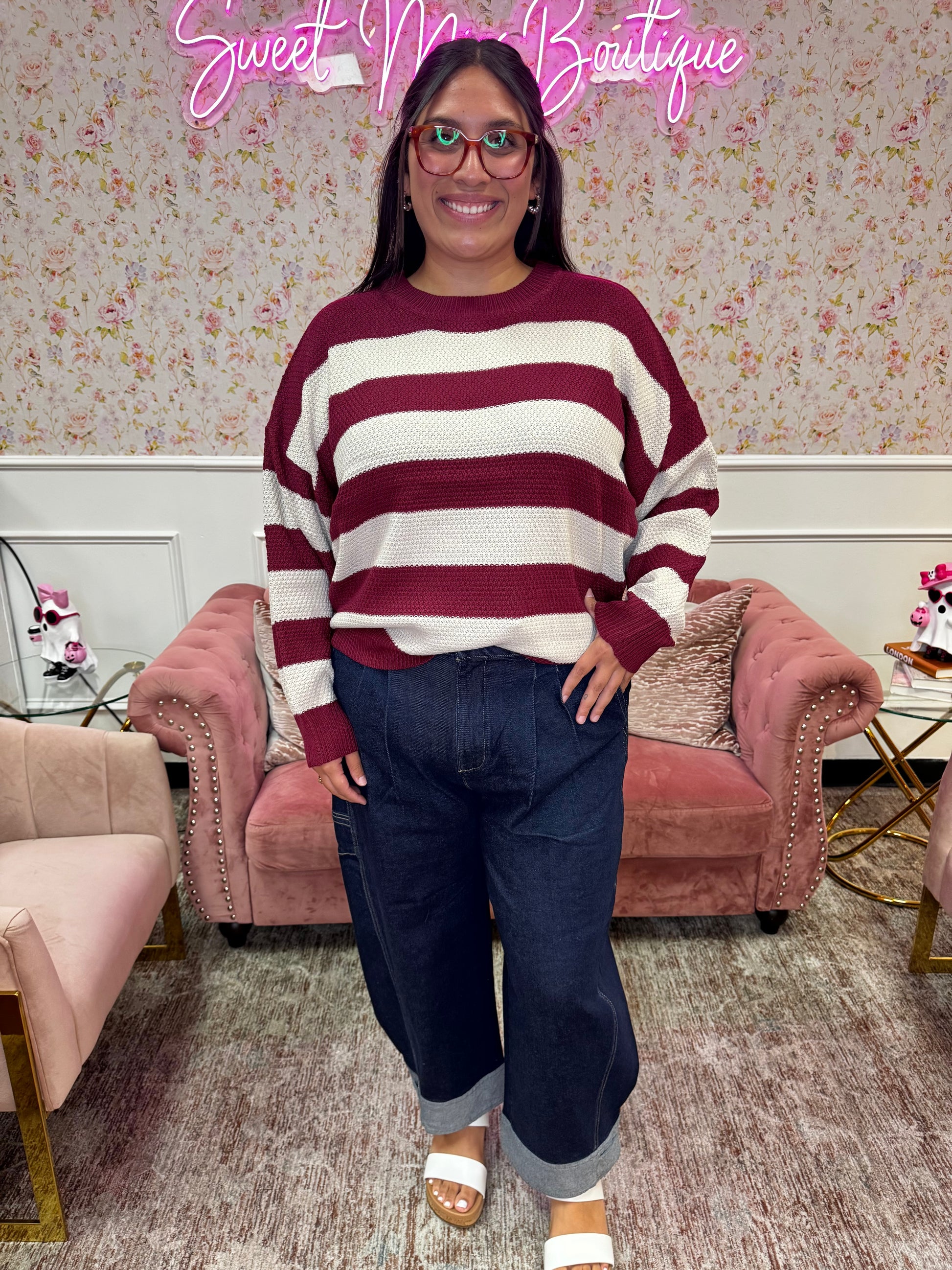 Woman modeling a burgundy and cream striped long sleeve knit sweater with dark wash cuffed wide-leg jeans.