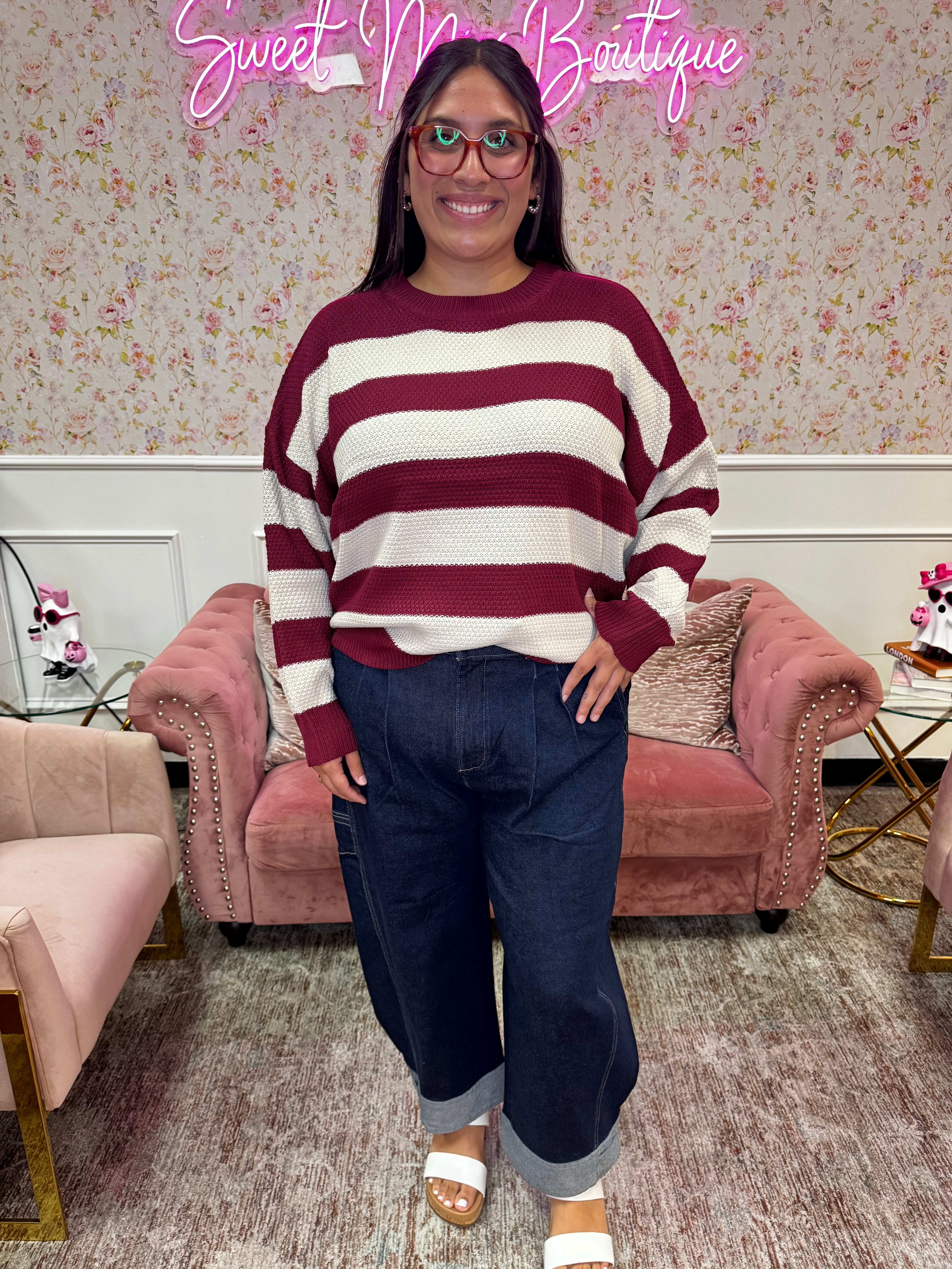 Woman modeling a burgundy and cream striped long sleeve knit sweater with dark wash cuffed wide-leg jeans.