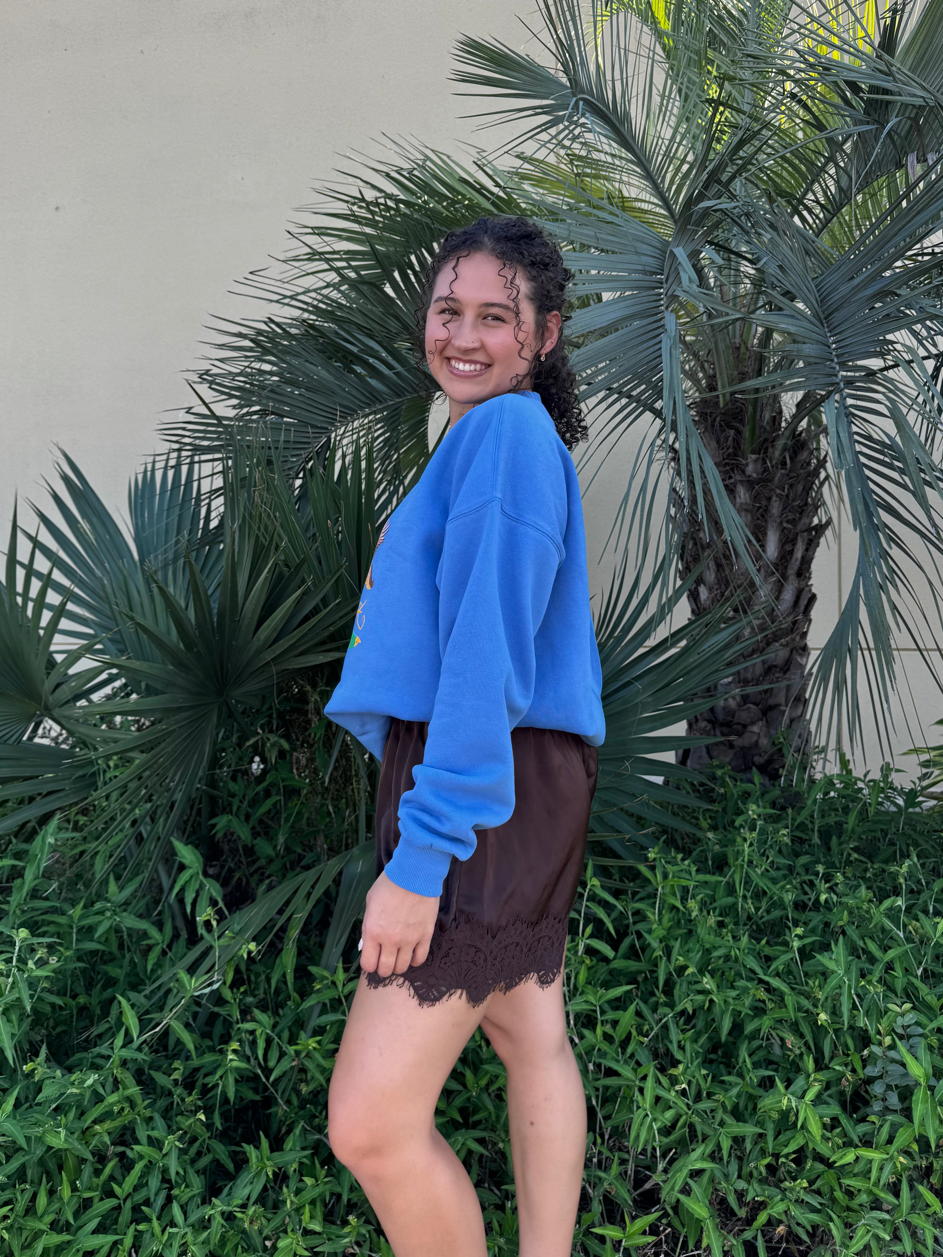 Close-up of woman in blue duck graphic sweatshirt with palm leaves background, showcasing the vibrant design and casual style.