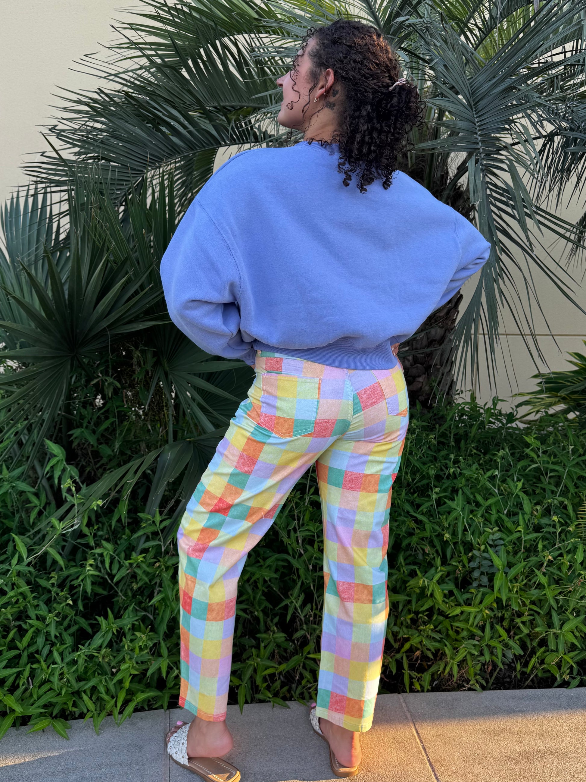 Woman with curly hair in blue sweatshirt featuring a colorful duck graphic, wearing a beaded necklace, standing outdoors.