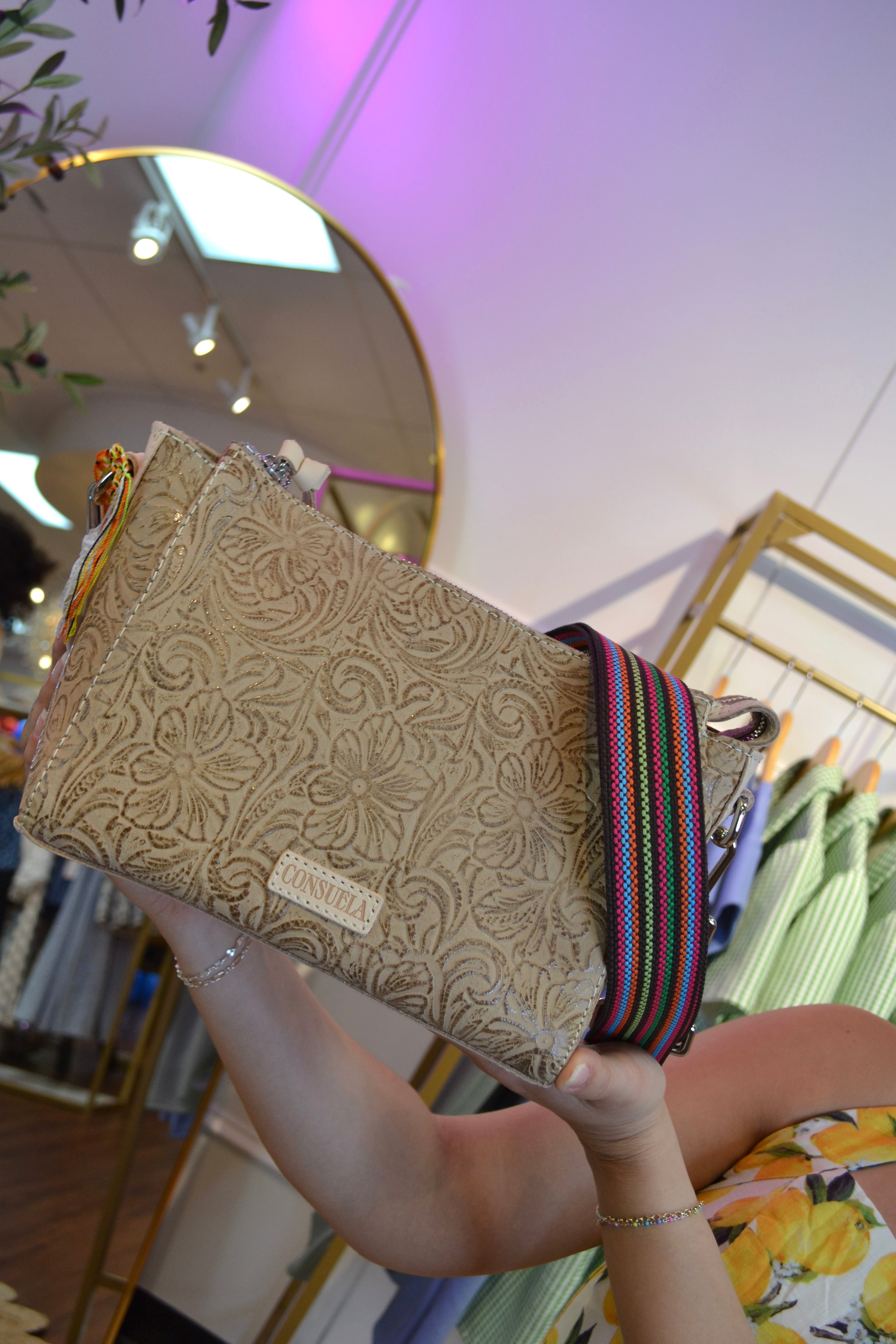 Beige Consuela crossbody bag with intricate floral tooled leather design, adjustable strap, and a small front label