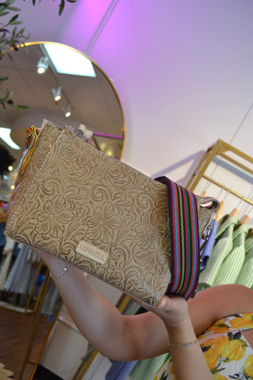 Beige Consuela crossbody bag with intricate floral tooled leather design, adjustable strap, and a small front label