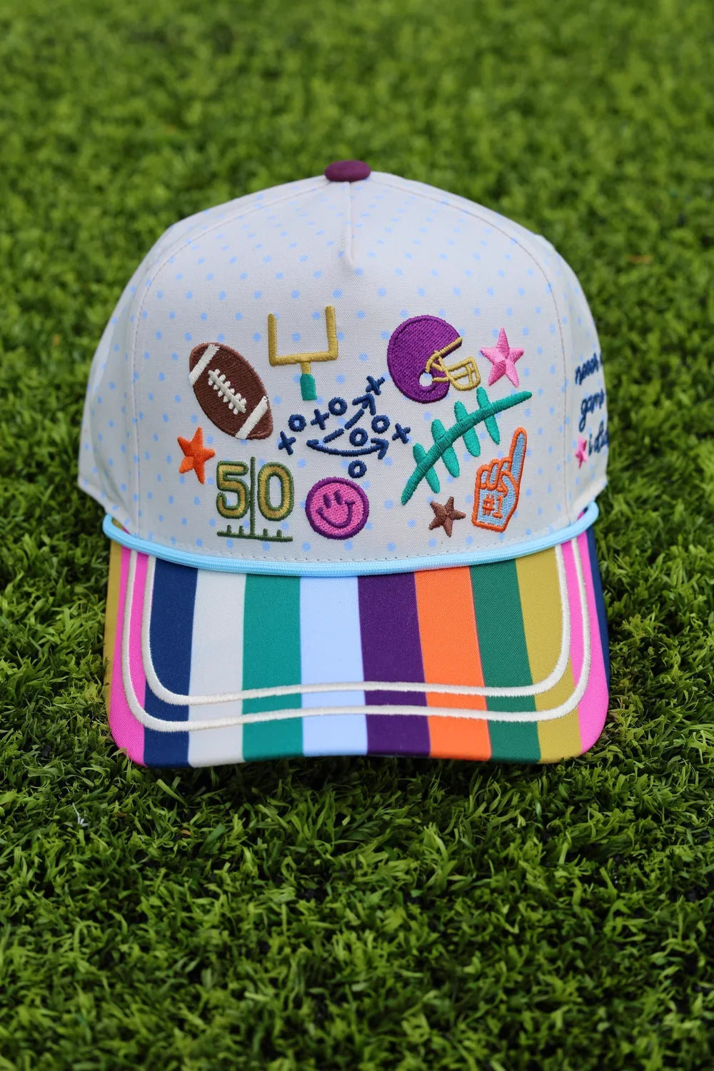 White baseball cap with colorful embroidered football, star, and sports-themed designs, rainbow striped brim, perfect for game day