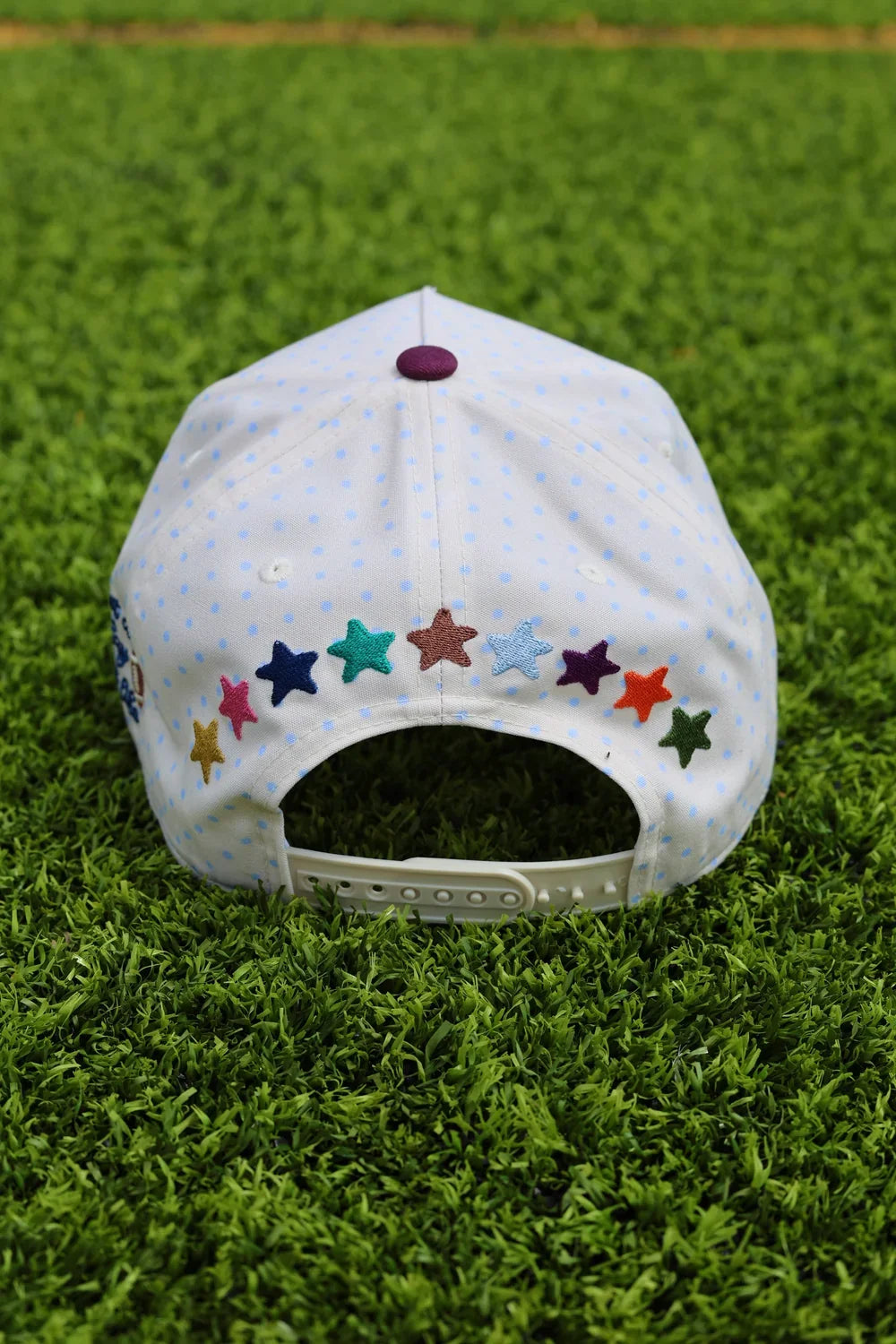 White baseball cap with colorful star embroidery, purple top button, adjustable strap, on green grass, perfect for casual wear