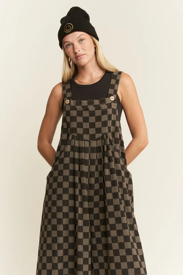 Close-up of woman wearing wide leg checkerboard overalls with black sleeveless top and black beanie, looking at camera.