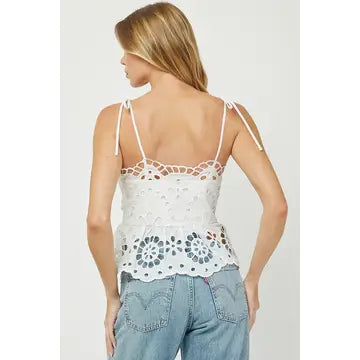 Woman wearing a white lace top and blue jeans on a plain background