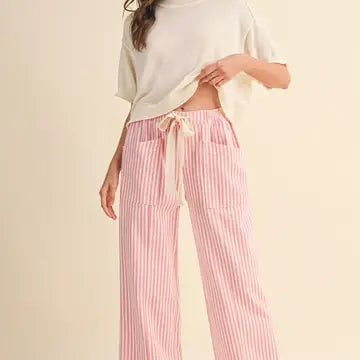 A model wearing pink and white vertically striped wide-leg pants with a cream drawstring waist, paired with a cream t-shirt, against a solid light beige background.