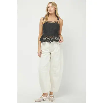 Woman wearing a black lace top and white pants on a light gray background