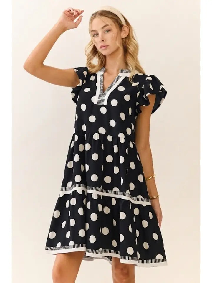woman wearing black and white polka dot tiered dress with flutter sleeves and contrast trim detail