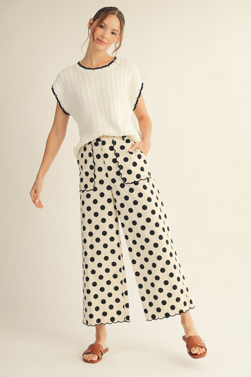 Woman wearing a white top with black trim and polka dot pants on a beige background