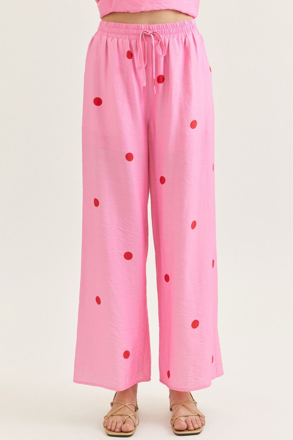 Pink polka dot pants made of lightweight fabric with red dots, elastic waistband with drawstring, wide-leg style, perfect for casual wear