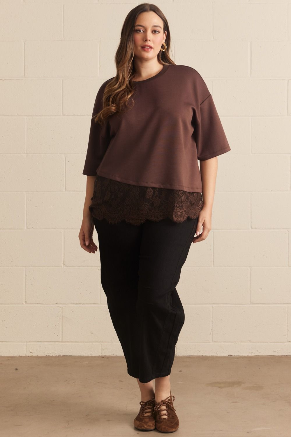 Model wearing plus size brown lace asymmetrical tee with lace hem, paired with black pants, side view highlighting fit
