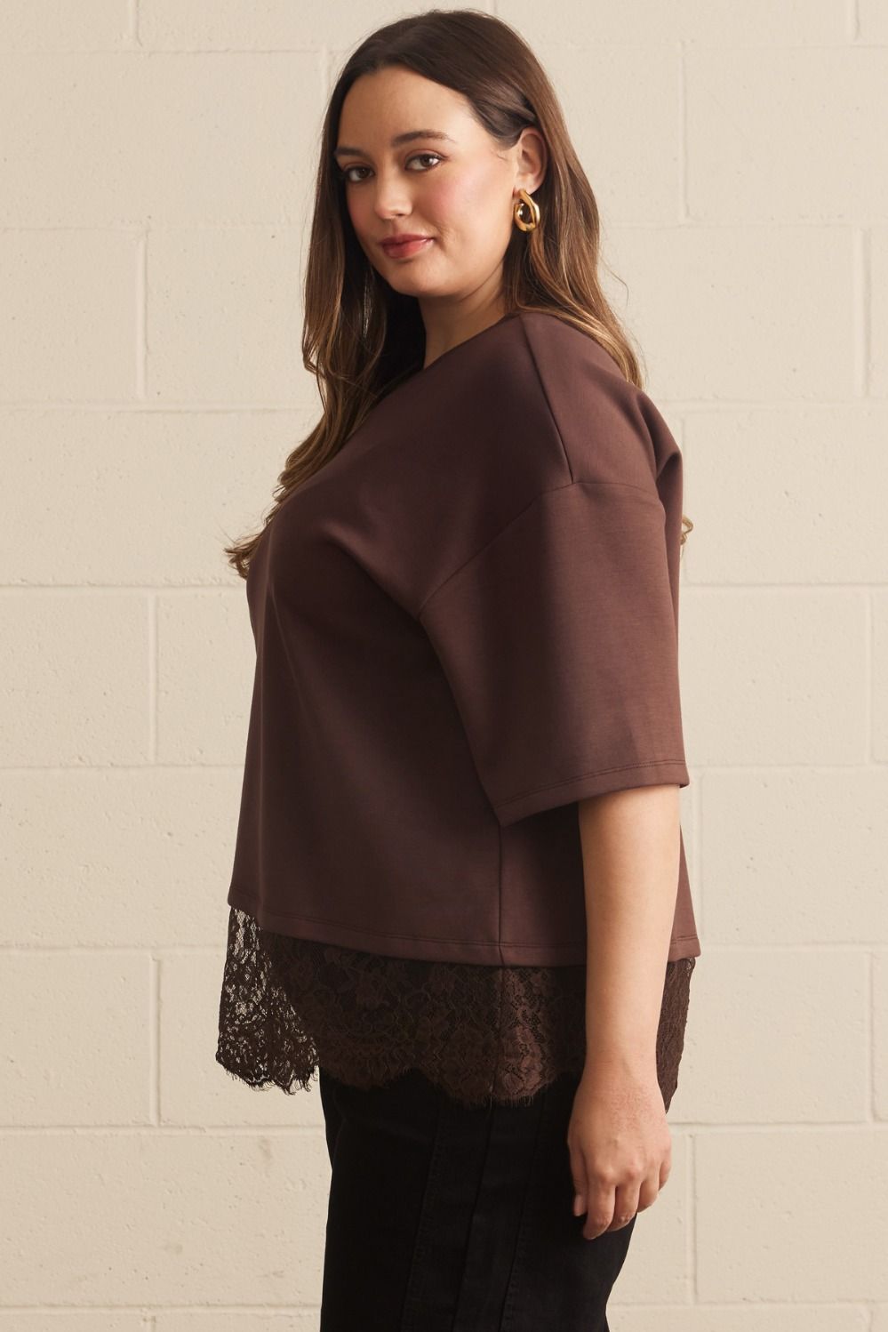 Model in brown lace asymmetrical tee with relaxed fit, showing front and side profile, paired with black pants and lace hem