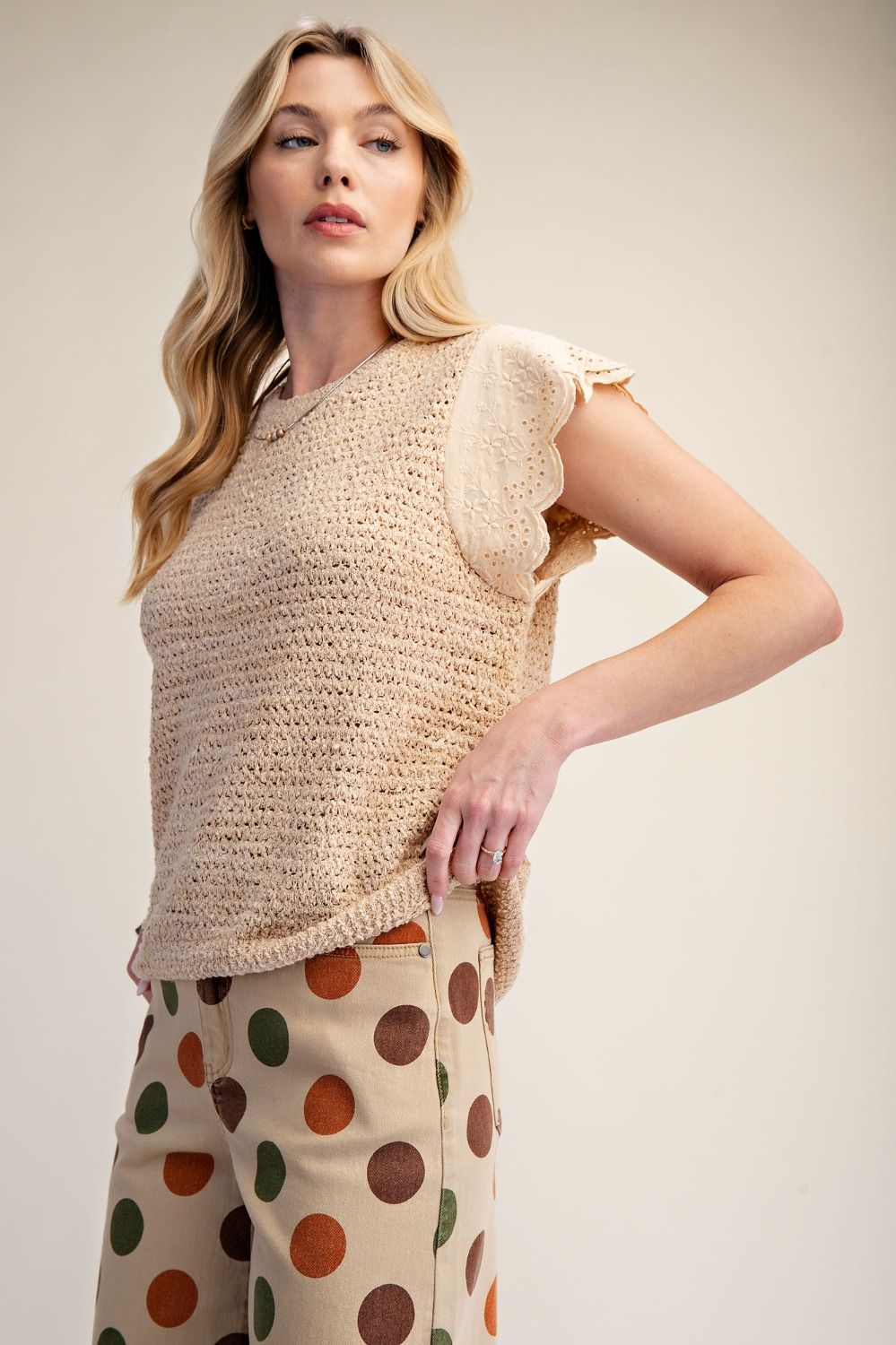 Light beige crochet knit top with scalloped eyelet flutter sleeves, paired with polka dot beige and brown pants, casual chic style