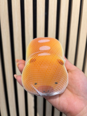 Orange capybara squishy toy with a soft, squeezable texture, small face details, held in hand against a wooden slat background, perfect for stress relief and sensory play.
